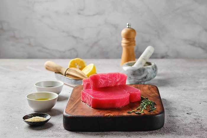 Raw ahi tuna steak on cutting board with spice and herbs, by Aleksei Isachenko