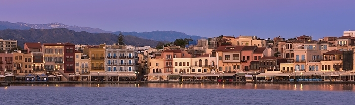 Sunrise or sunset over Old Venetian port and harbour promenade of Chania, Crete, Greece. Shops, restaurants, hotels of the port marina. Soft purple, blue to pink sky and distant Cretan mountains. Panoramic shot, by Natallia Pershaj
