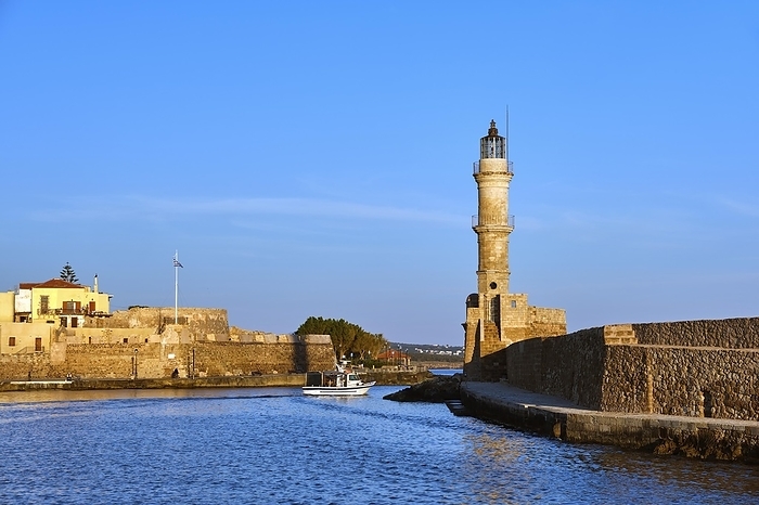 Fishing boat passing by famous Lighthouse and walls of old port, Firka fortress of Old Venetian harbour of Chania, Crete, Greece in early morning. Golden hour shot. Clear blue sky and sea, by Natallia Pershaj