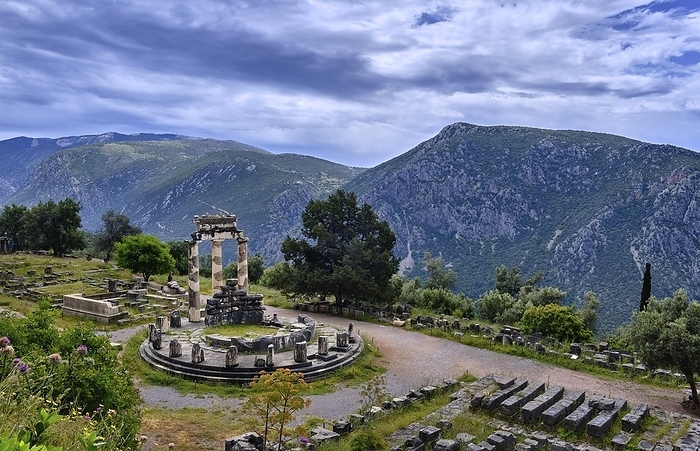 Ruins of Tholos of ancient Greek goddess Athena Pronaia in Delphi, Greece. Three Doric columns with relieves on frieze of circular temple on slope of sacred mount Parnassos and next to famous Delphi complex. UNESCO World heritage site. Wide downshot, by Natallia Pershaj
