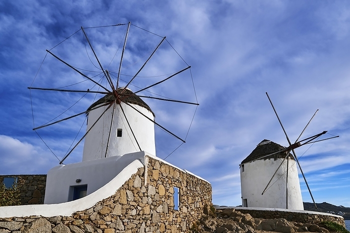 Famous tourist attraction of Mykonos, Cyclades, Greece. Two traditional whitewashed windmills by waterfront and Chora town. Summer, blue sky, beautiful clouds. Travel destination, iconic view. Frontal shot, by Natallia Pershaj