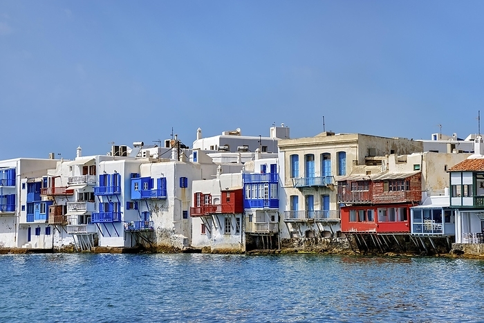 Seafront Little Venice of Mykonos main town or Chora, Cyclades, Greece. Romantic neighborhood with bars, cafes, restaurants in whitewashed old fisherman houses hanging on cliffs above sea waves. Summer day, clear blue sky, by Natallia Pershaj