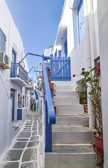 Charming traditional narrow streets and beautiful alleyways of Greek island towns. Whitewashed houses, flower pots, blue balconies, stairs and doors, cobble paved street. Summer day sunshine. Mykonos, Greece, Europe, by Natallia Pershaj
