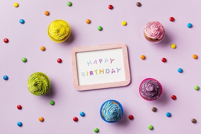 Happy birthday slate surrounded with colorful gems muffins pink background, by Oleksandr Latkun