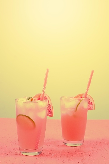 Fresh pink alcoholic cocktail with grapefruit lemon slice ice cubes against yellow background, by Oleksandr Latkun