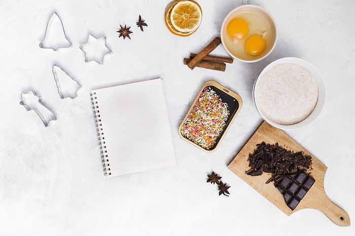 Spiral notepad with colorful sprinkles pastry cutter star anise cinnamon dried citrus egg yolk chocolate bar white backdrop, by Oleksandr Latkun