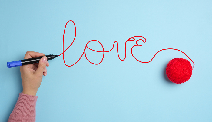 A woman s hand wrote love with a red felt tip pen and a ball of wool on a blue background. A woman s hand wrote love with a red felt tip pen and a ball of wool on a blue background.