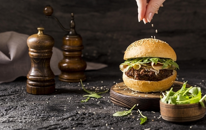 Front view hand pouring sesame seeds beef burger with salad bacon, by Oleksandr Latkun