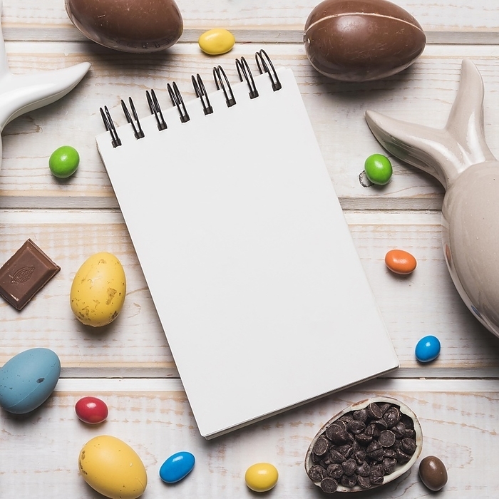 Overhead view blank spiral notepad with easter eggs candies choco chips wooden desk, by Oleksandr Latkun