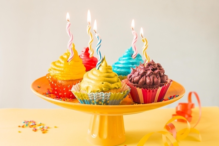 Close up colorful muffins with illuminated candles cakestand, by Oleksandr Latkun