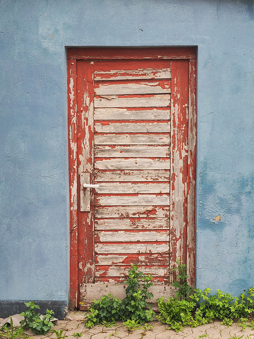 red door with paint flaking off in a red wall red door with paint flaking off in a red wall, by Zoonar Katrin May