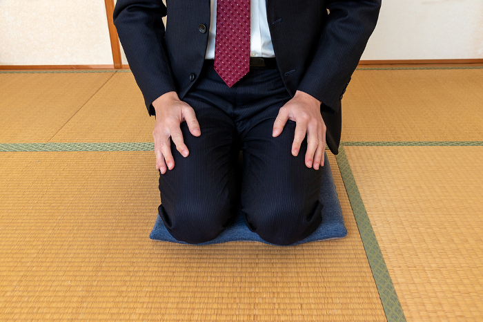 A man in a suit sitting seiza on a zabuton (Japanese-style cushion) in a Japanese-style room