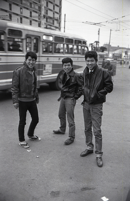 Trendy Japanese Youngsters Three young Japanese men wearing trendy hairstyles, jeans and leather jackets, in an imitation of the American Greaser look, stand on a street in Tokyo as a city bus passes, 1960  Showa 35 .                 Photo by MeijiShowa AFLO