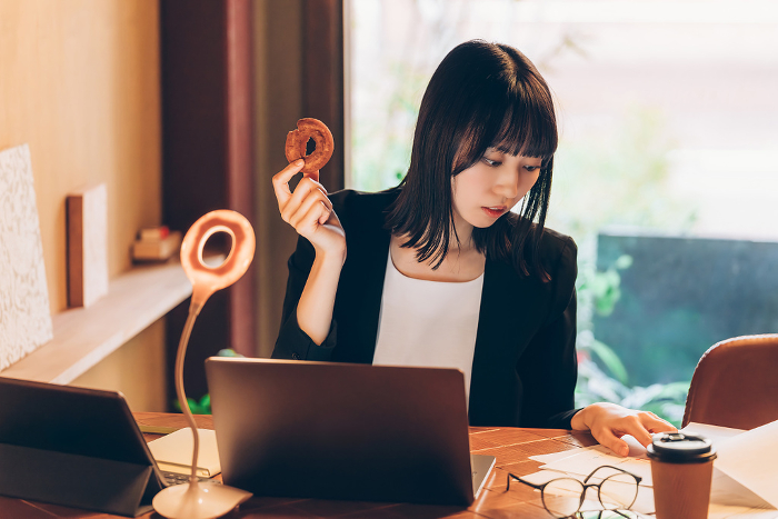 Japanese woman using a computer while eating a doughnut (People)