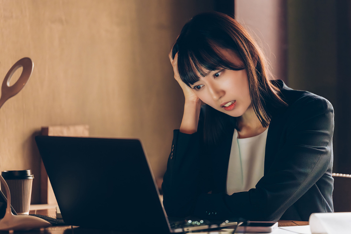 A Japanese businesswoman worries by holding her head down while using a computer (People)