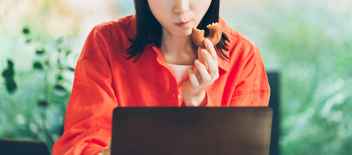 Woman using computer while eating donut
