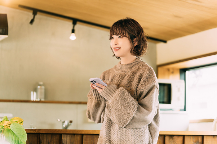A Japanese woman in knitwear using her phone with a smile on her face (People)