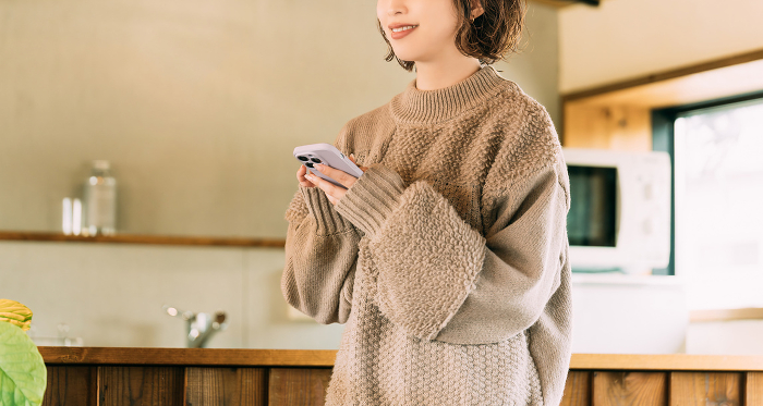 Woman in knitwear using a phone with a smile on her face.