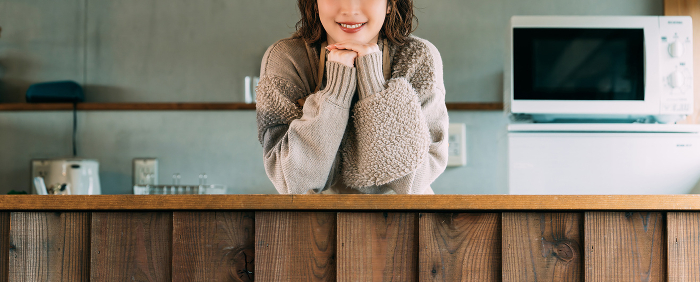 A smiling Japanese woman resting her elbows on the kitchen counter.