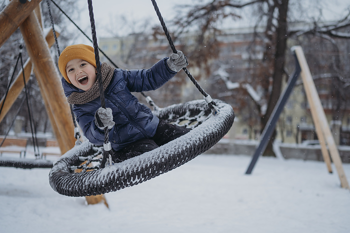 Happy boy swinging on nest swing in winter park