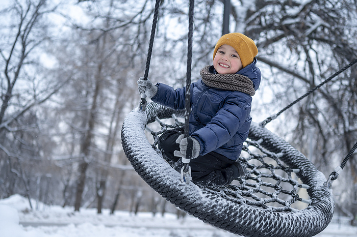 Smiling boy swinging on nest swing in winter park