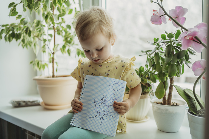 Girl sitting on window sill and showing drawing