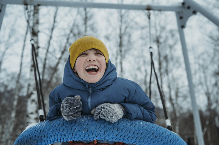 Happy boy swinging and enjoying on tire swing in winter park