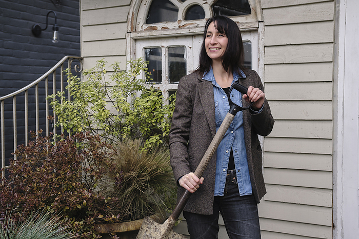Smiling woman holding shovel in front of house