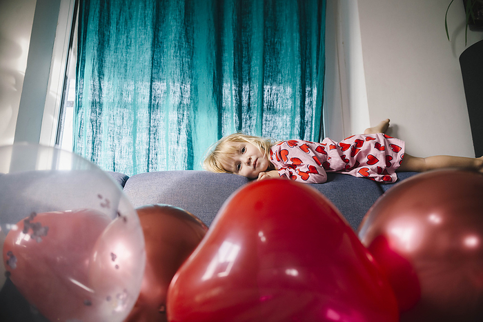 Sad girl lying on sofa with balloons at home