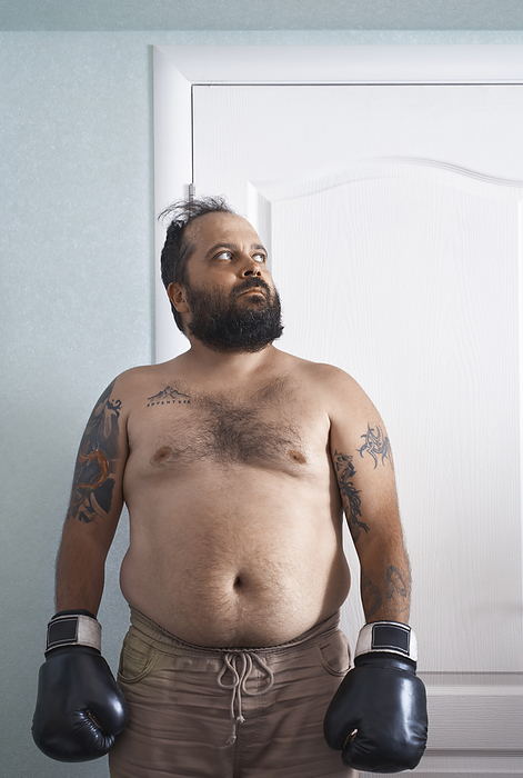 Mature overweight man wearing boxing gloves and standing at home
