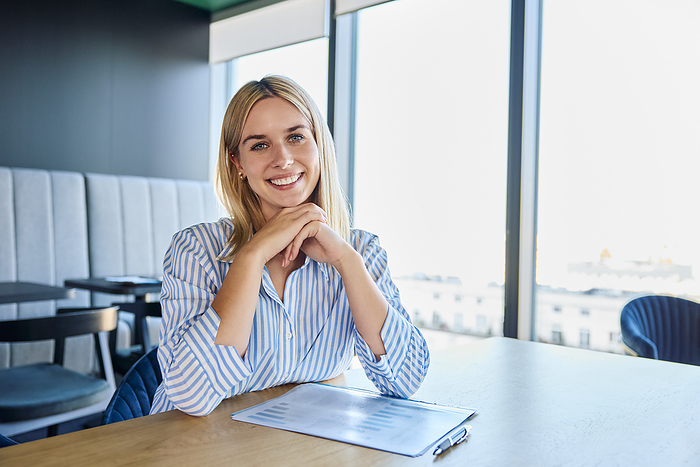 Smiling blond businesswoman sitting with graph at desk