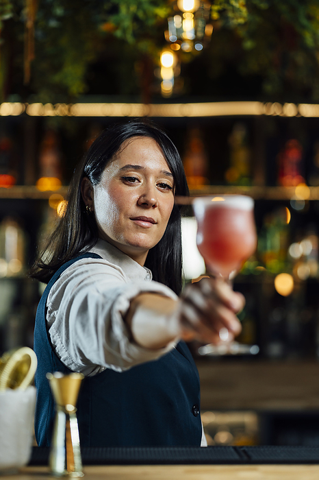 Confident bartender holding cocktail drink in bar