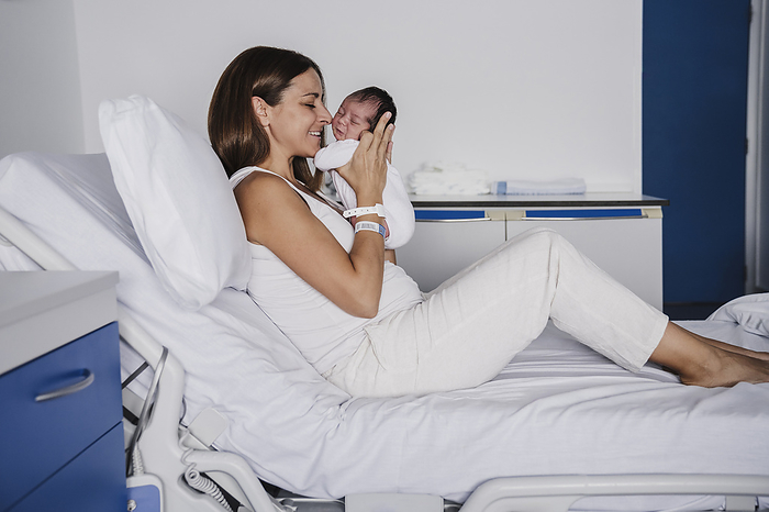 Loving mother embracing baby daughter on bed in hospital