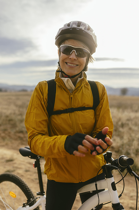 Smiling woman standing with mountain bike at field