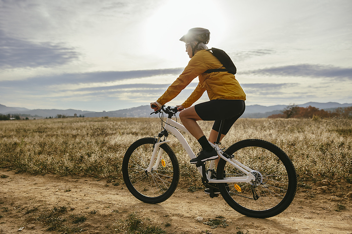 Woman riding mountain bike near field at sunset