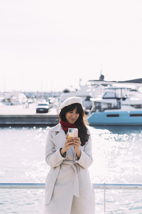 Smiling woman using smart phone at harbor