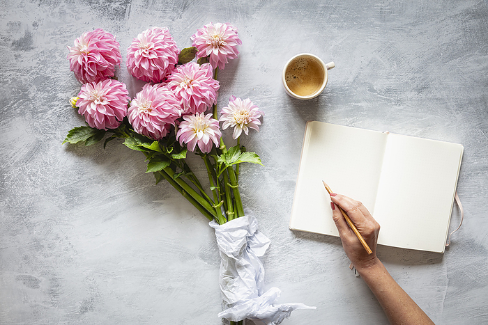 Hand of woman writing in diary in front of bouquet of pink blooming 
