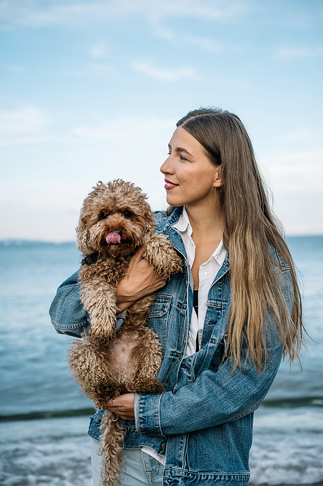Smiling young woman with poodle dog standing at beach