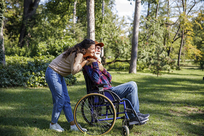 Happy caregiver embracing retired senior man in wheelchair at park