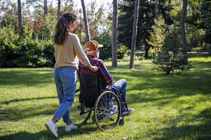 Caregiver pushing retired senior man in wheelchair at park