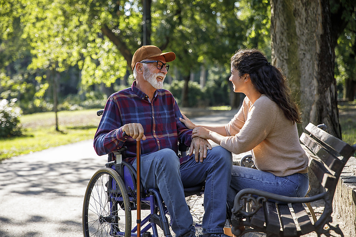 Happy retired senior man in wheelchair talking with volunteer