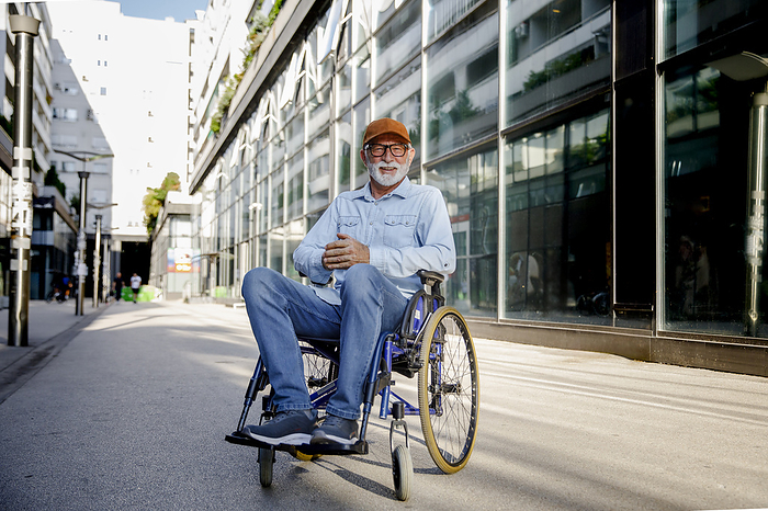 Smiling retired senior man with hands clasped sitting in wheelchair on footpath