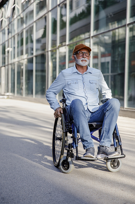 Retired senior man sitting in wheelchair on footpath