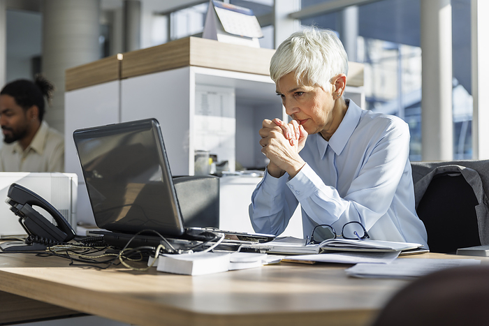 Worried businesswoman with hands clasped looking at laptop in office