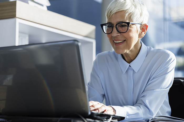 Happy businesswoman wearing eyeglasses and using laptop at office