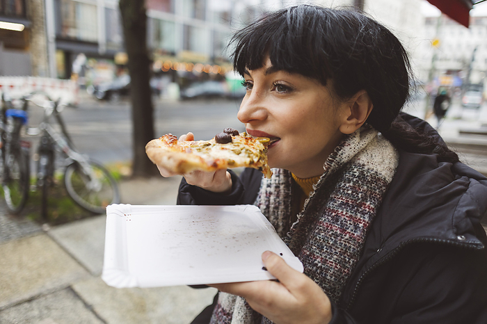 Happy woman eating slice of pizza at sidewalk cafe