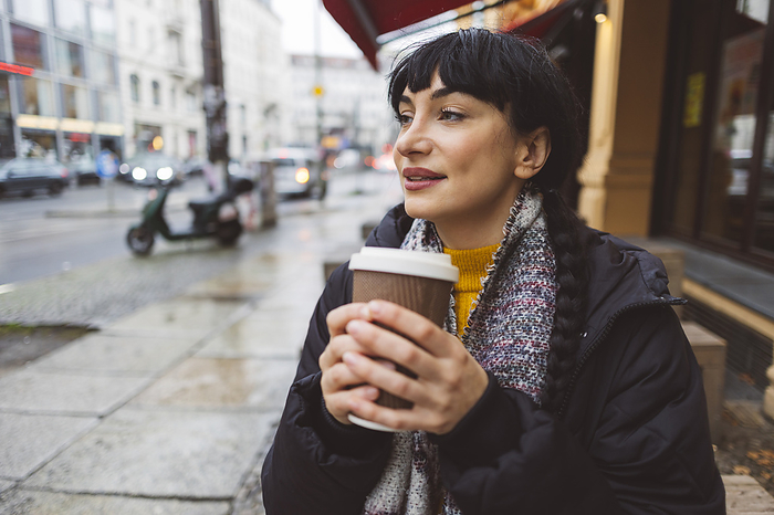 Smiling beautiful woman holding disposable coffee cup at street