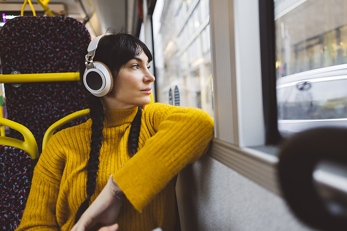 Thoughtful woman wearing wireless headphones and sitting in bus