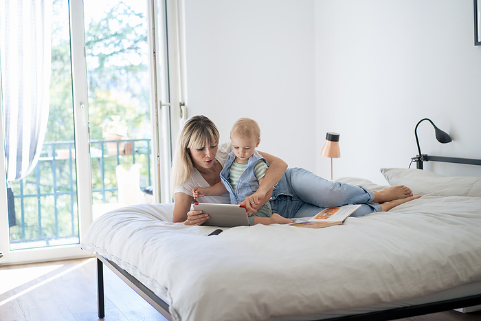 Mother lying on bed and using tablet PC with son at home