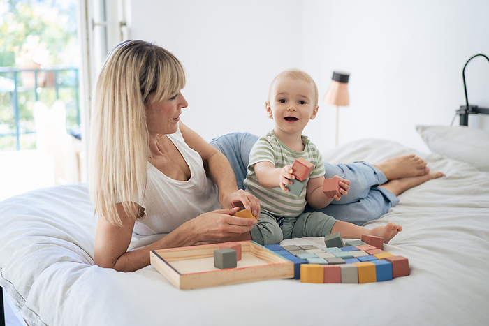 Mother and son playing with toy blocks on bed at home